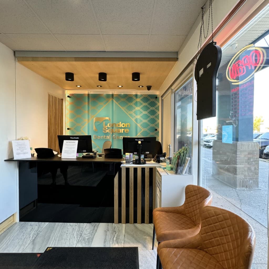 Modern reception area of London Square Dental Centre featuring a teal branded feature wall, professional desk, and comfortable leather waiting chairs